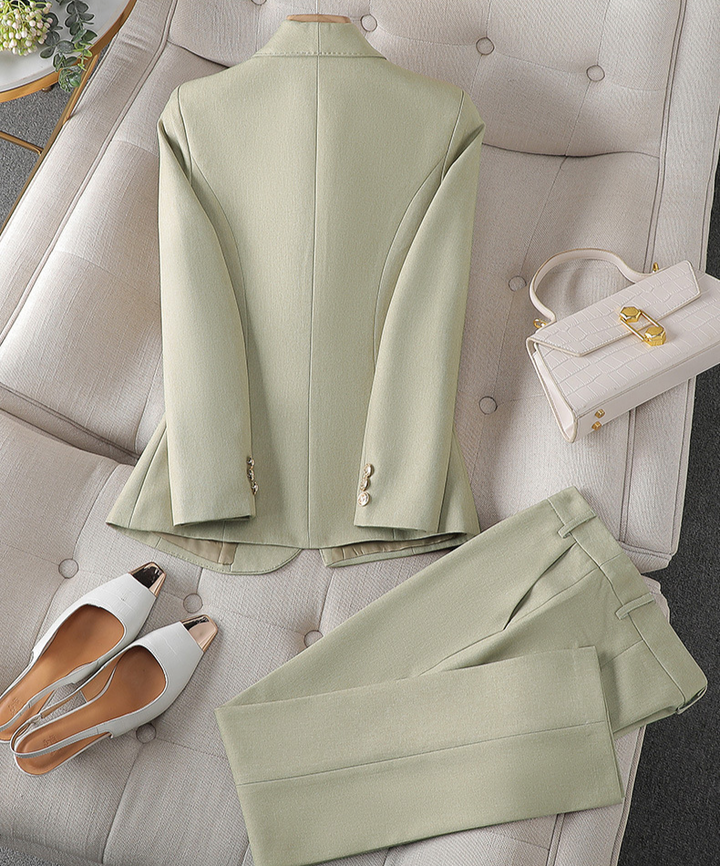 Ein stylischer hellgrüner Blazer und eine passende Hose auf neutralem Untergrund, dazu eine kleine Handtasche und ein Paar weiße Sandalen.